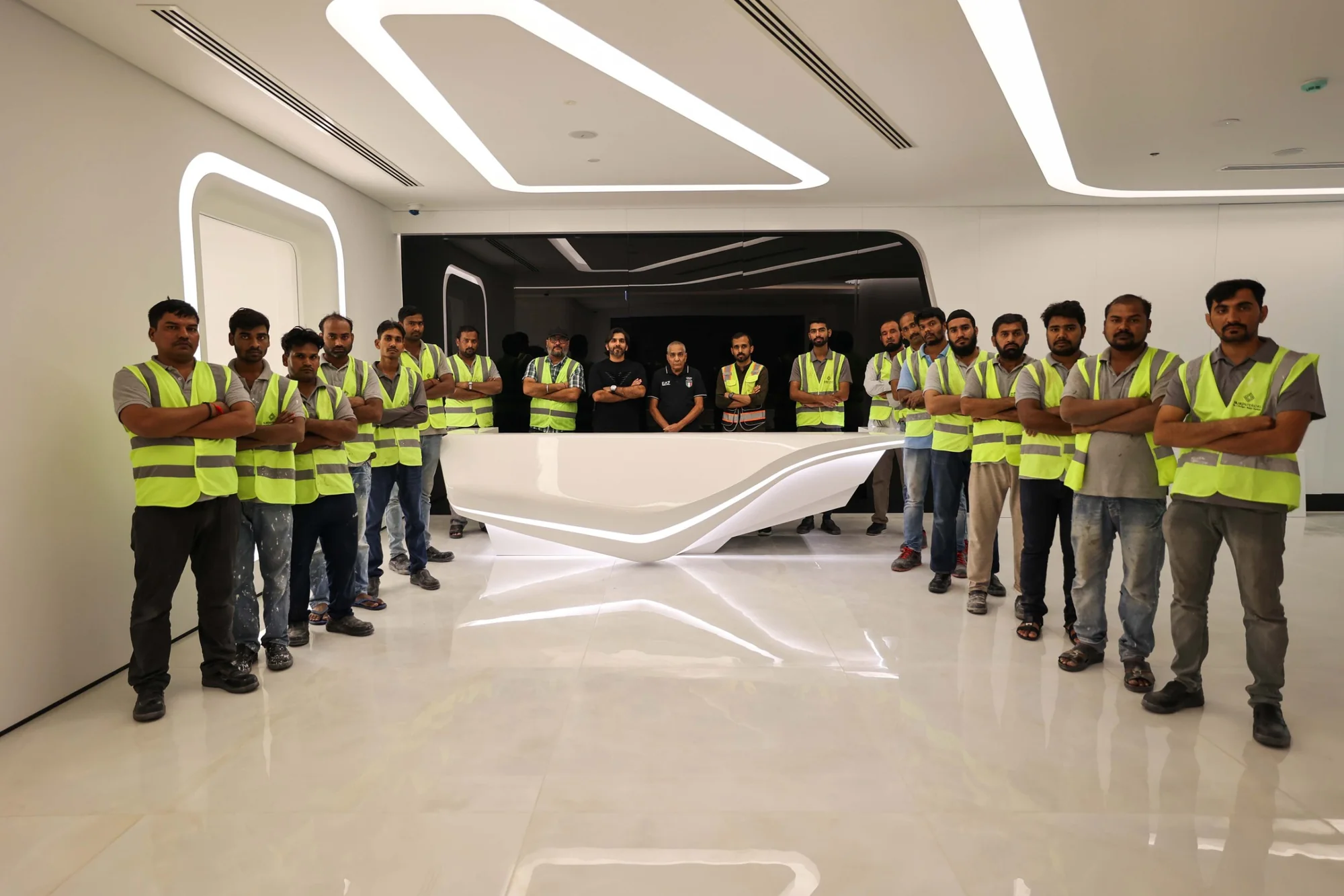 The Fajr Interiors team, more than twenty people, most in Fajr hi-vis vests, standing with arms folded around a white curved reception desk in a finished office