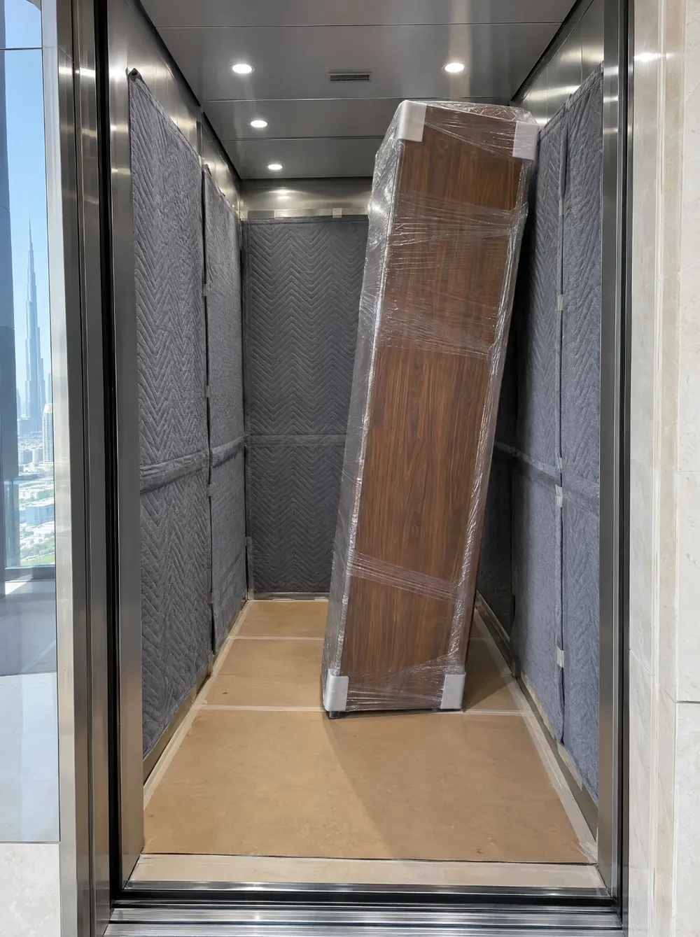 Concept visualisation: a padded service-lift car in a Dubai tower, with a wrapped walnut wardrobe panel tilted inside it