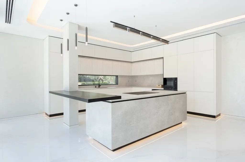 Photograph: the kitchen as built at Cluster 39, Villa 1, Jumeirah Islands, with the stone-clad island, dark counter, fluted panels and linear pendant