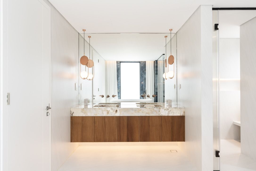 A rebuilt villa bathroom by Fajr: a floating walnut vanity with stone top under pendant lights
