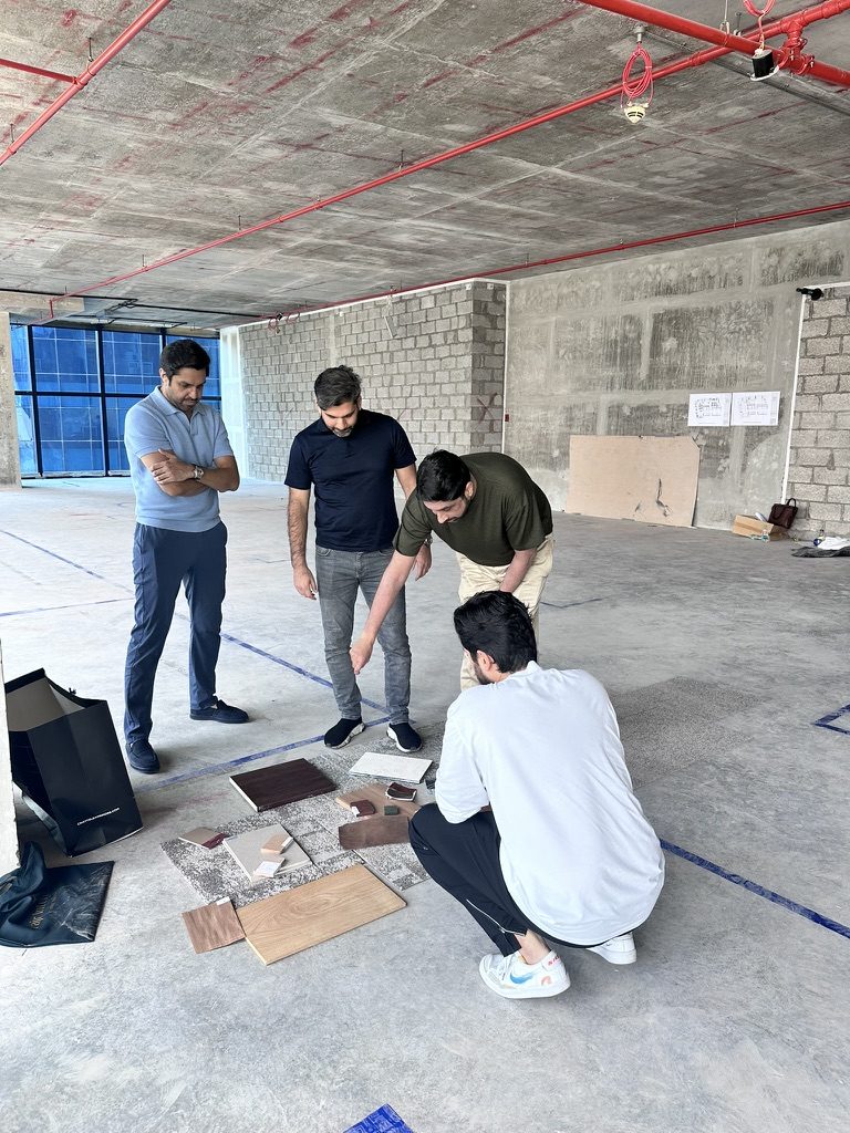 Fajr Interiors design team laying out timber, stone and carpet samples on the bare concrete floor of the Opus Tower office