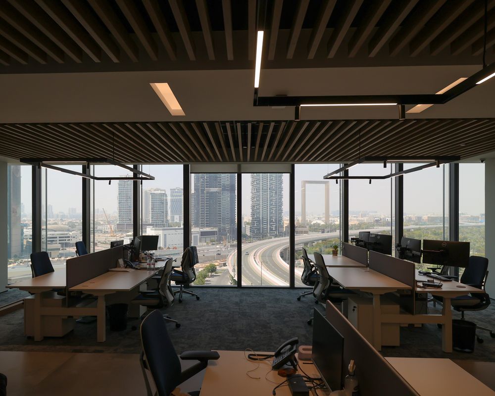 Task lighting at IMI, One Za'abeel: rows of desks under linear lights against a city-view window wall