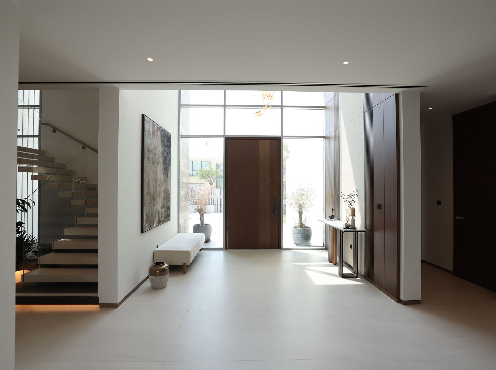 Double-height villa entrance with a pale stone floor, walnut panelling, a pivot front door and a floating stair, delivered by Fajr Interiors, Dubai