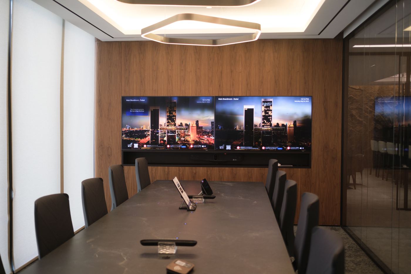 Boardroom with a long stone table, timber wall and twin screens, delivered by Fajr Interiors, Dubai
