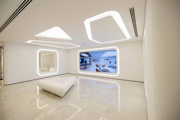 Open area at Crypto One: lit ceiling rafts, framed display niches and a glossy white stone floor