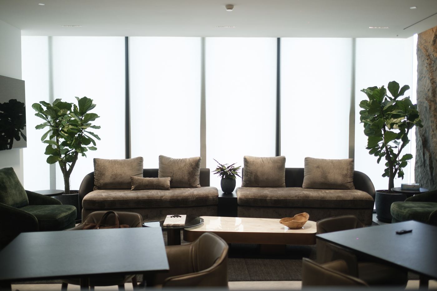 Staff lounge with velvet sofas, café tables and planting by full-height windows, delivered by Fajr Interiors, Dubai