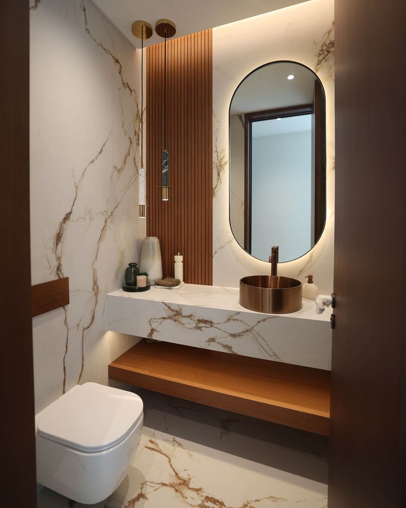 A rebuilt bathroom by Fajr: marble walls, a walnut panel, an oval lit mirror and a floating vanity