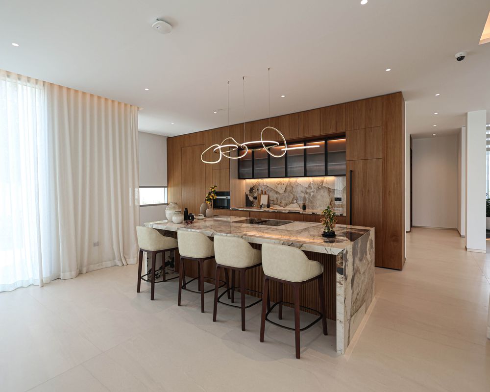 Kitchen at Villa 47 Fairways, Dubai Hills: a marble waterfall island and walnut tall units