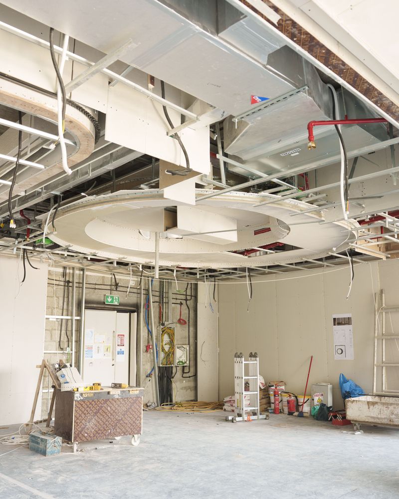An opened ceiling on a Fajr site: ducts, pipework and cable trays exposed, with the new ceiling framing going in