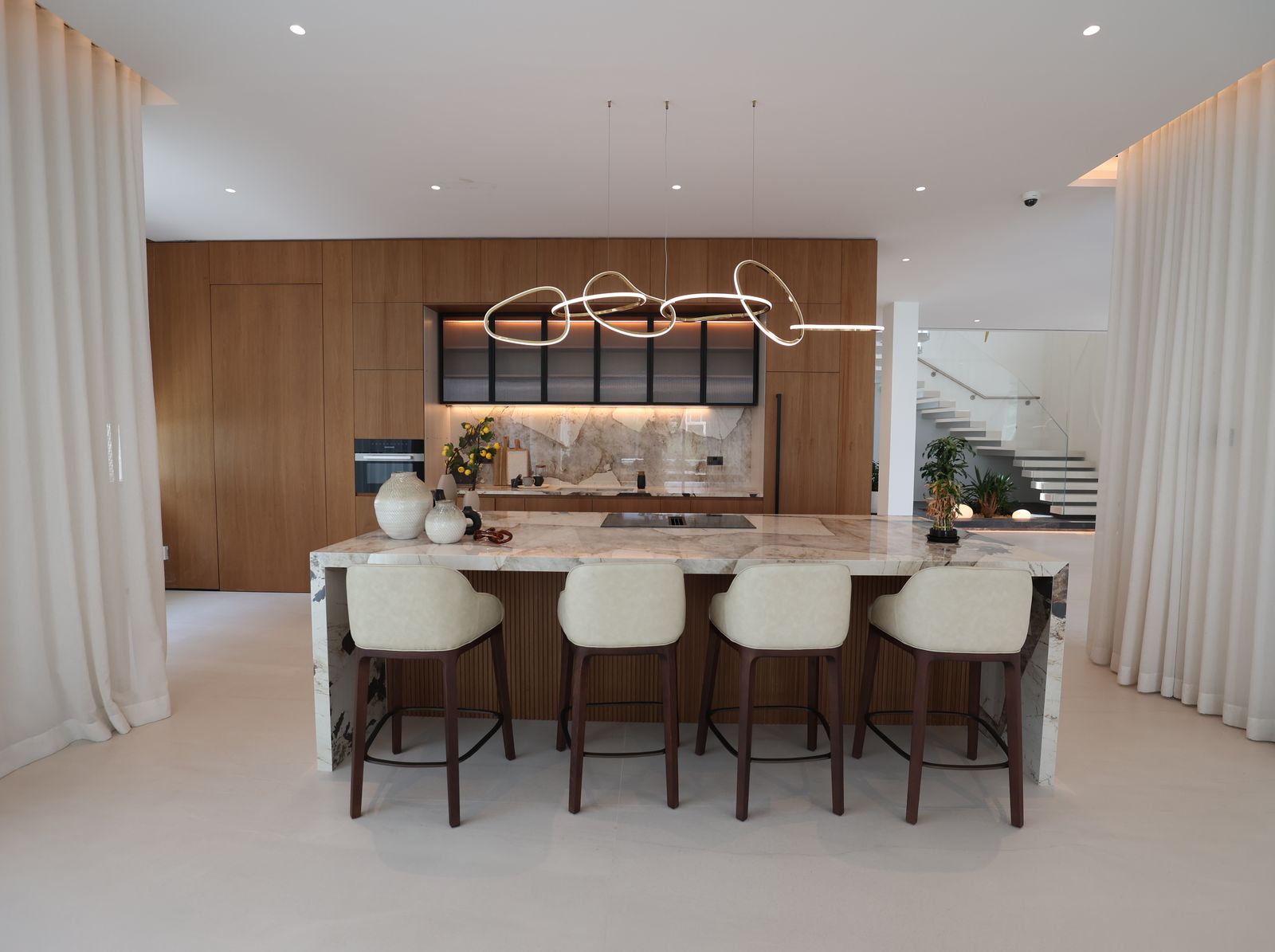 Villa kitchen with a marble island, walnut tall units, a ring pendant and leather bar stools, delivered by Fajr Interiors, Dubai