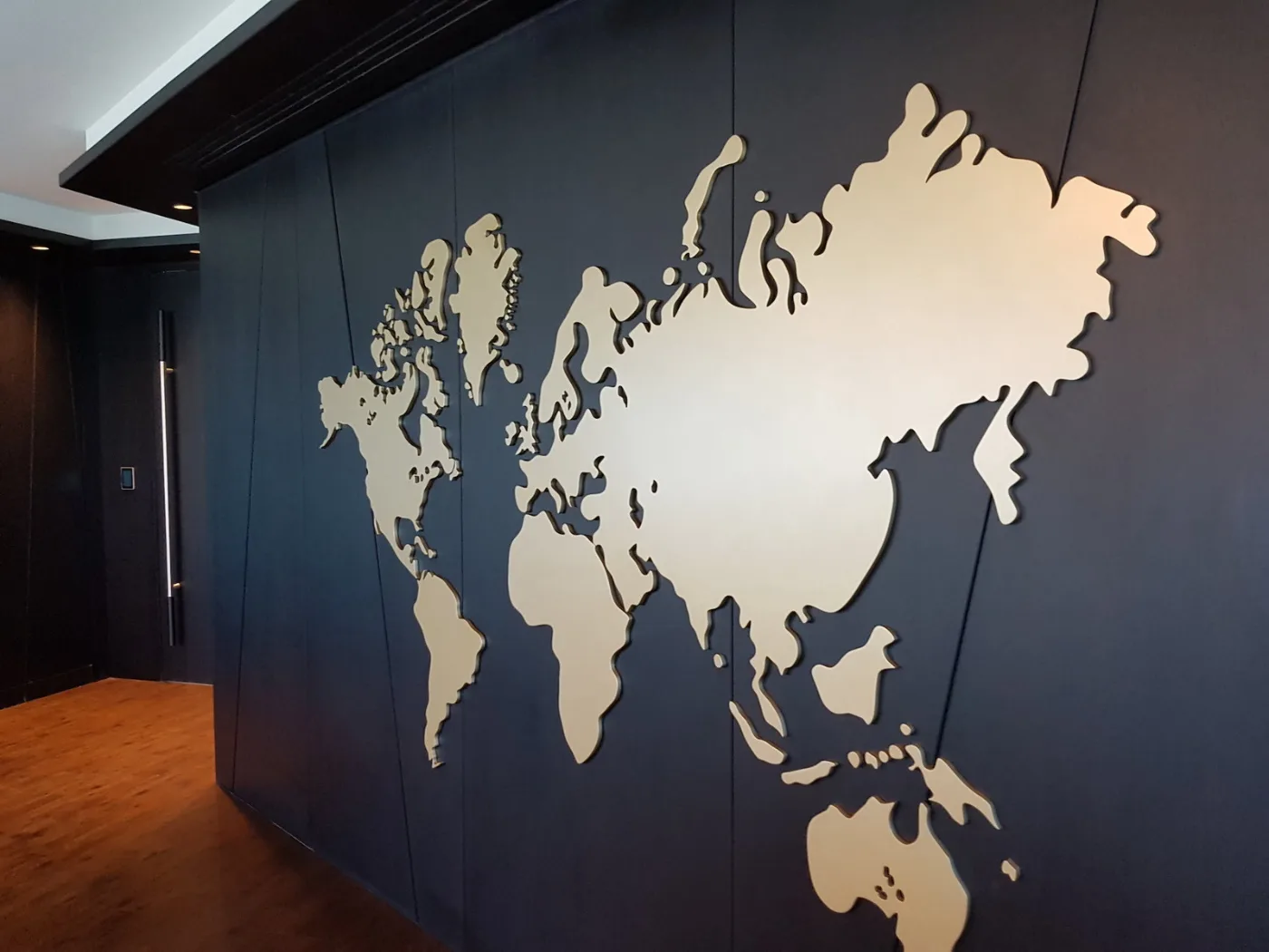 Brass world-map feature wall on dark panelling, delivered by Fajr Interiors for ASI, Dubai