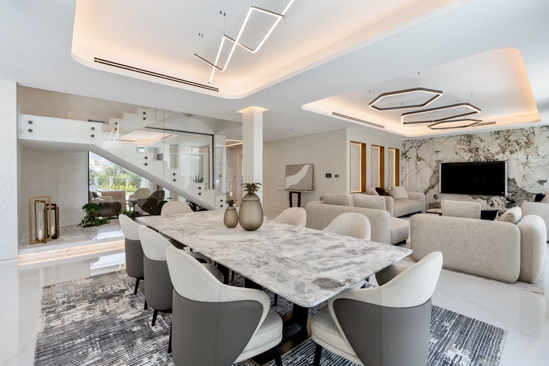 An upgraded villa living and dining room by Fajr Interiors: lit ceiling coffers, a marble feature wall and a stone dining table