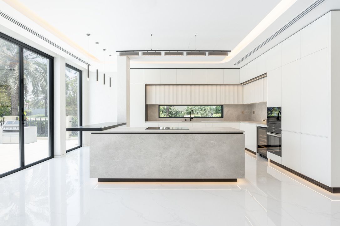 A villa kitchen opened up by Fajr: a stone island facing the garden glazing, handleless white units
