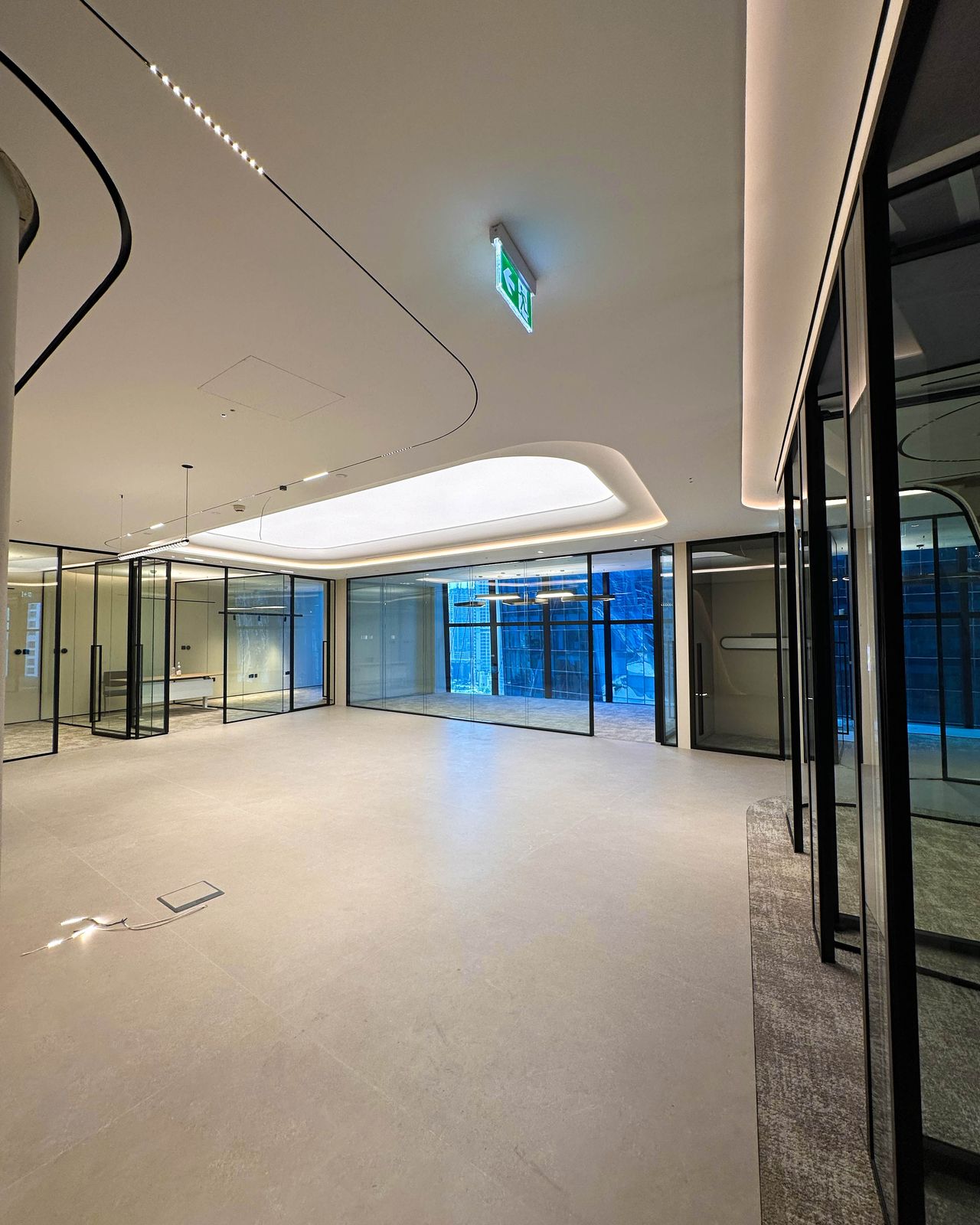 Open office floor at Opus by Omniyat: glass partitions along the core and a lit ceiling cove carrying daylight inward