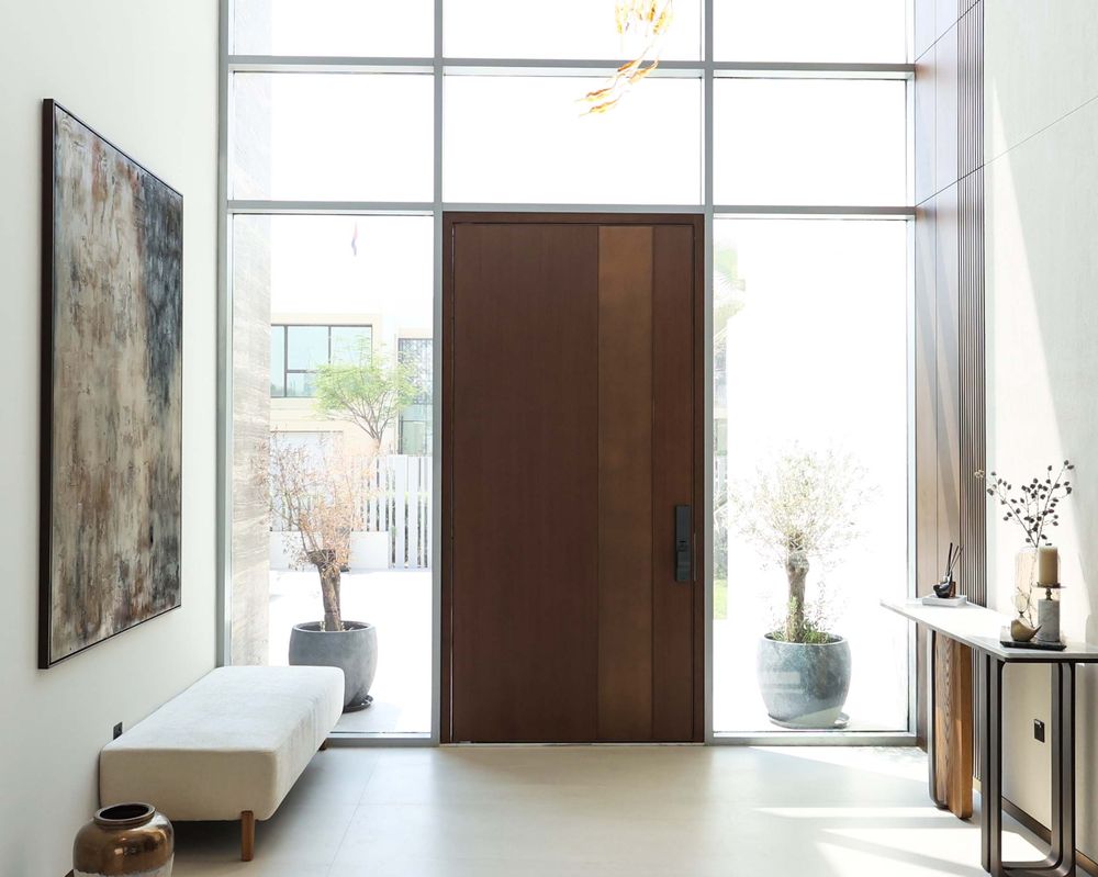 A walnut pivot entrance door in a double-height glazed hallway, by Fajr Interiors in Dubai Hills