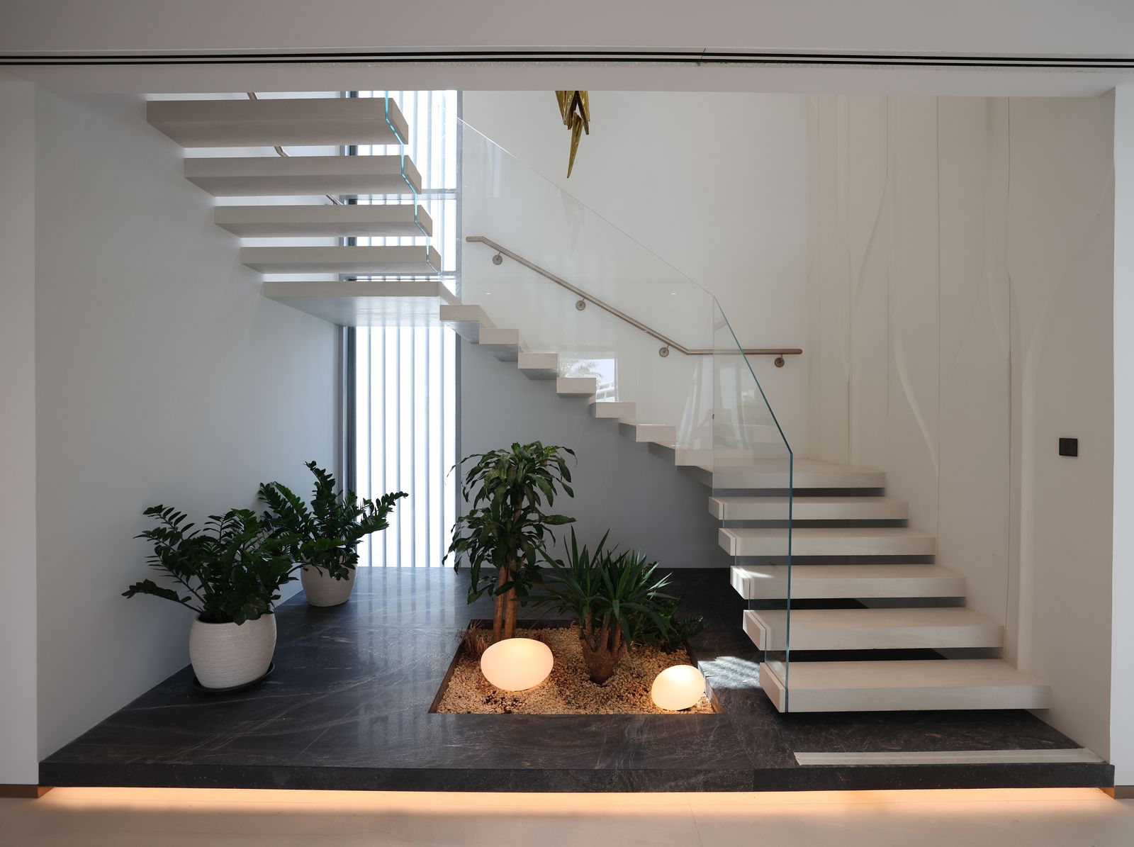 Floating stone stair with a glass balustrade over a planted void, delivered by Fajr Interiors, Dubai