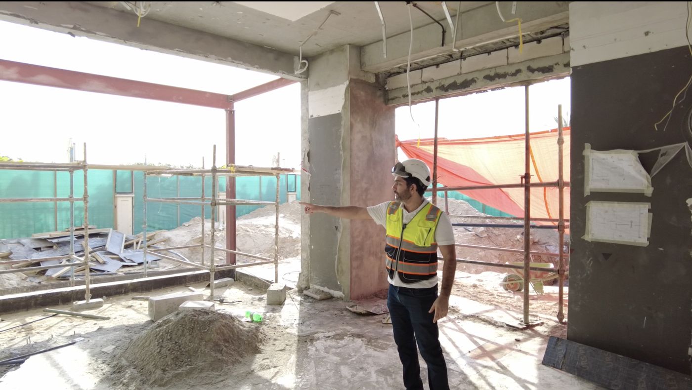 A Fajr site engineer pointing out a villa extension under construction, with the new structure and scaffold in place
