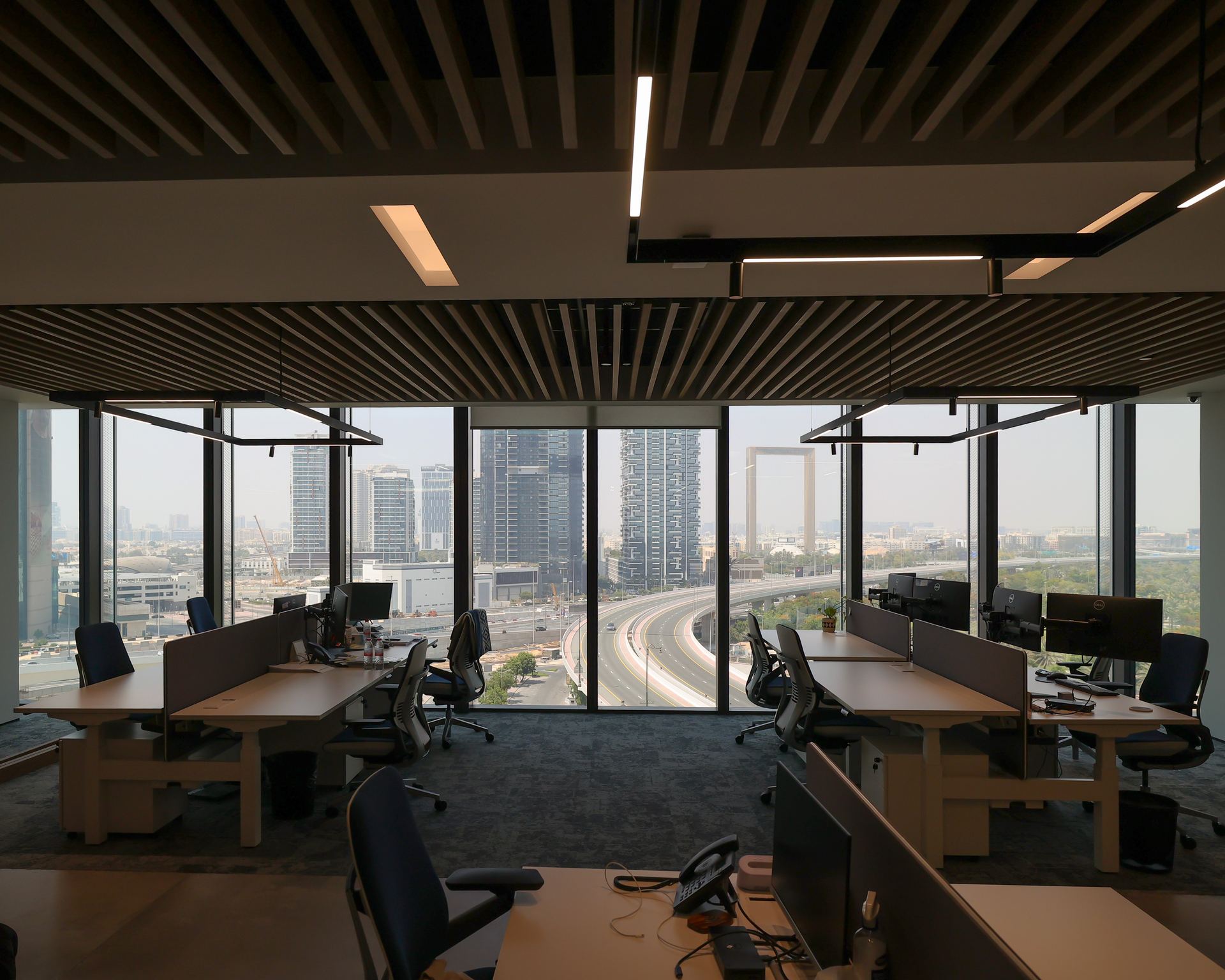 The IMI office at One Za’abeel by Fajr Interiors: workstations under timber ceiling slats and linear lights, the city through full-height glass