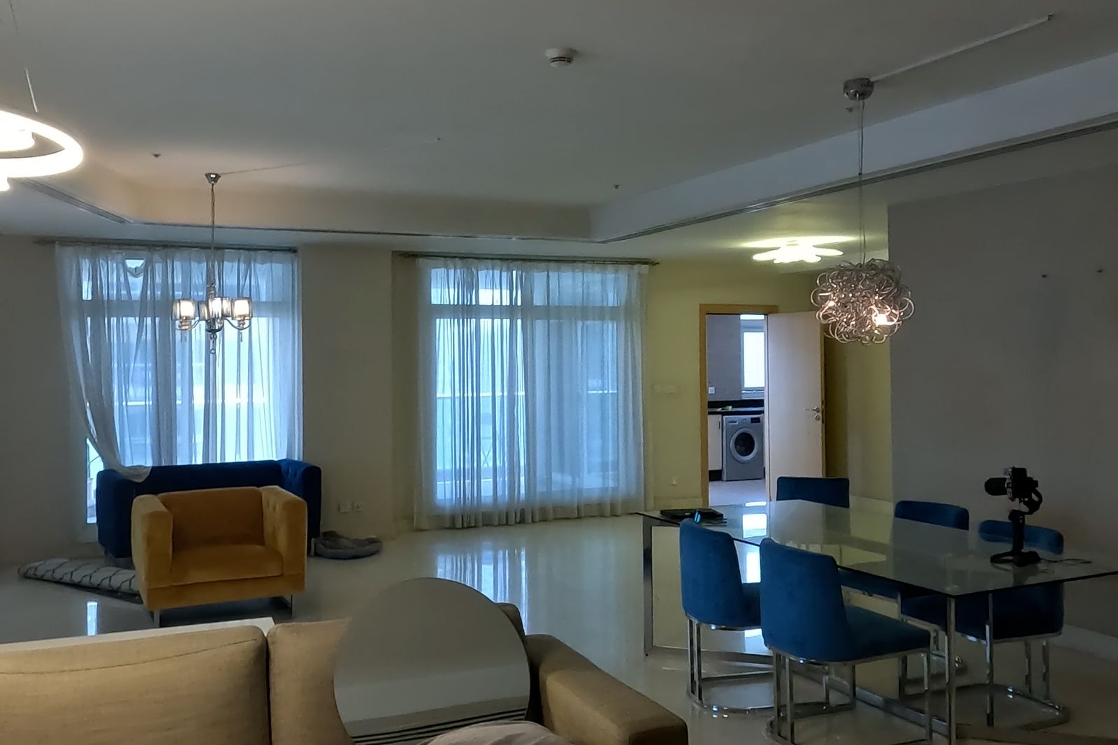 A Dubai Marina penthouse living room as found: floor-to-ceiling glass behind sheer curtains and a polished stone floor