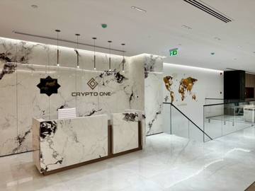 Reception at Crypto One: a book-matched marble wall with the Crypto One sign and a white stone desk