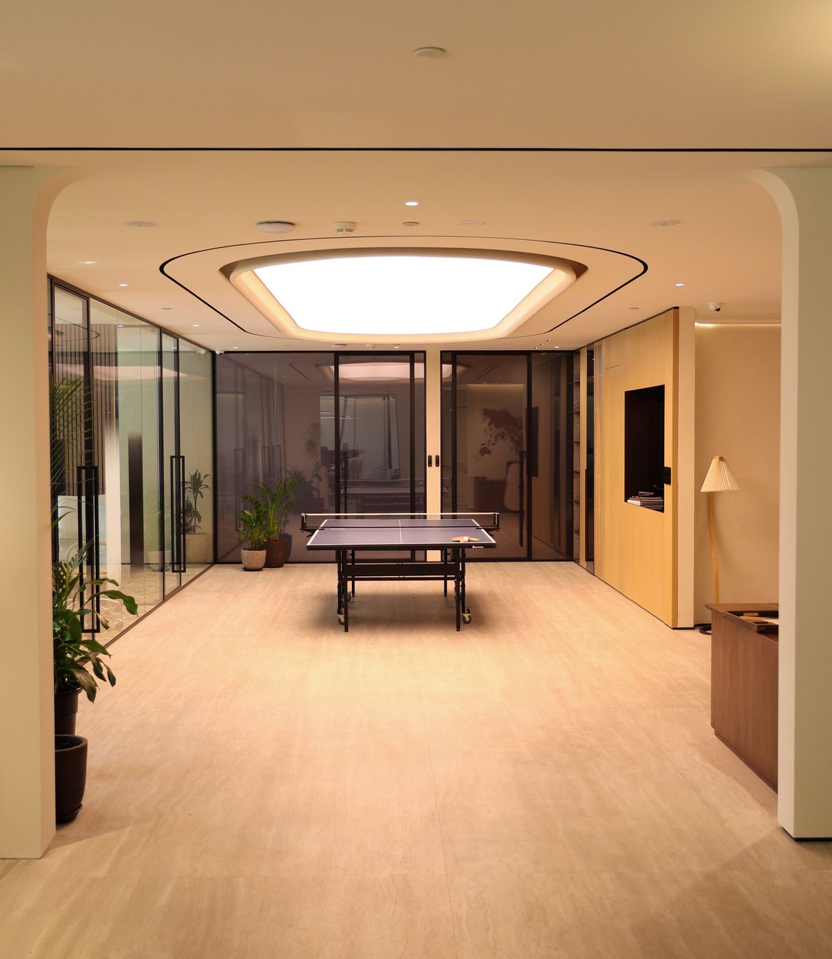 Finished breakout room on a Fajr Interiors office floor: timber wall joinery, glass partitions and a lit oval ceiling over a table-tennis table, Dubai