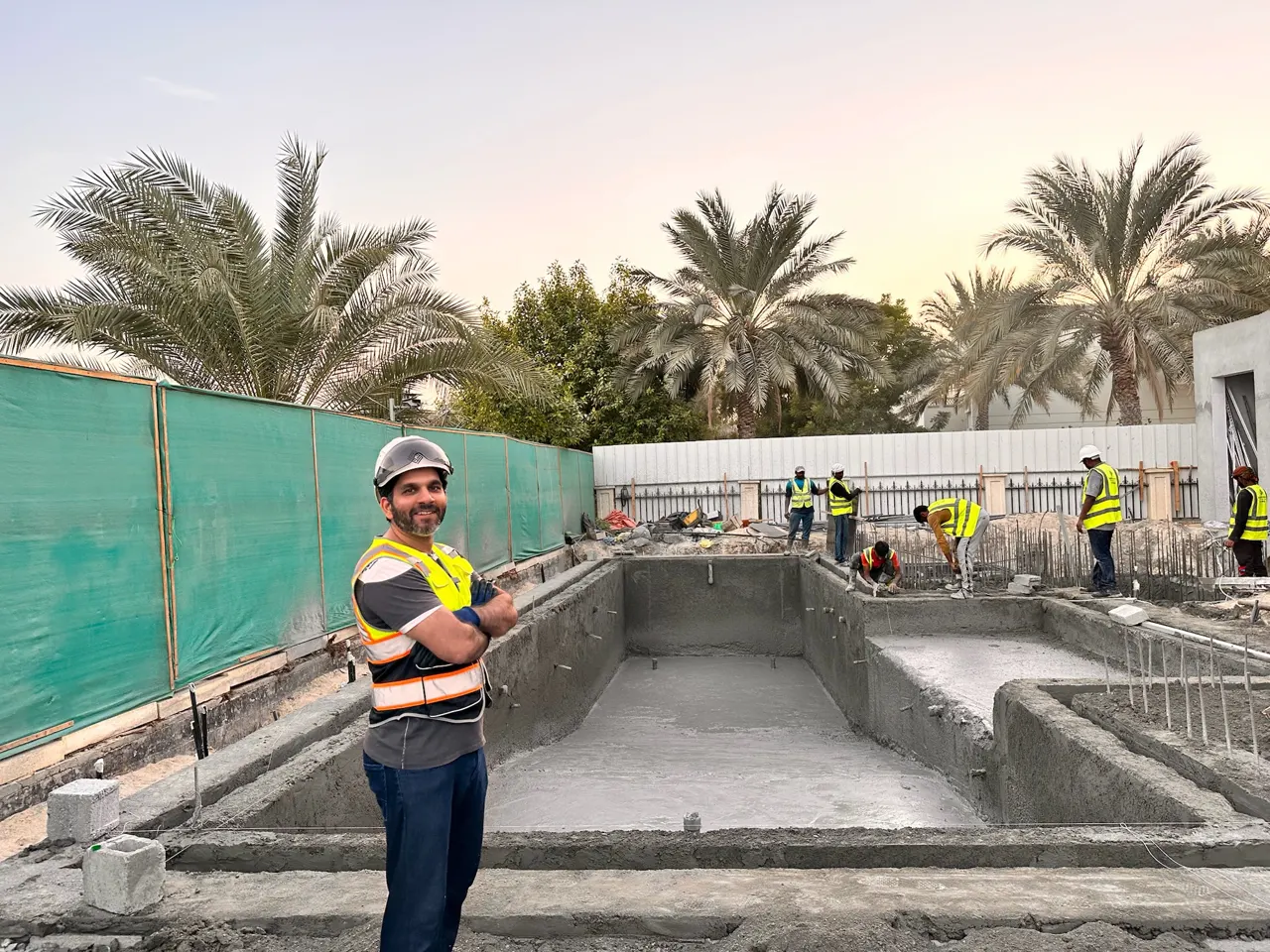 Photo: the pool shell, plastered in cement, with the crew at work and a man in a hard hat and hi-vis vest in front, Cluster 39, Villa 1, Jumeirah Islands