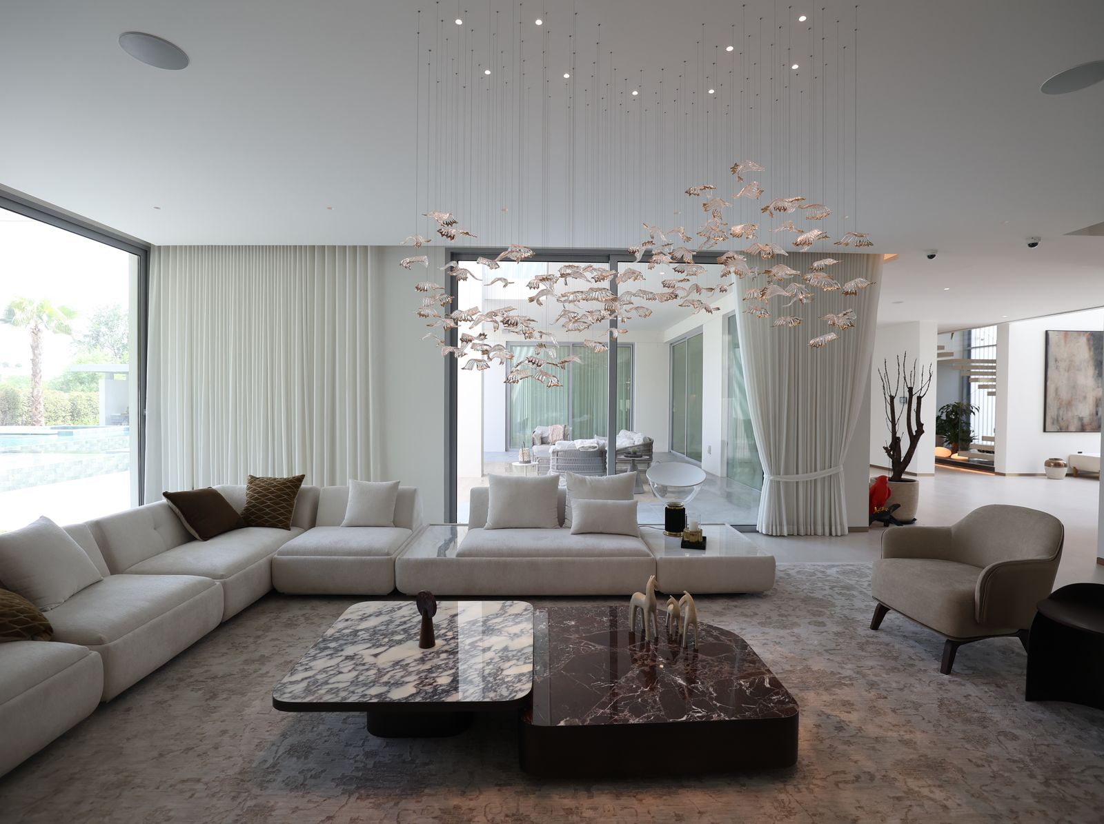 Villa living room with a low modular sofa, a marble coffee table, linen sheers and a leaf chandelier, delivered by Fajr Interiors, Dubai
