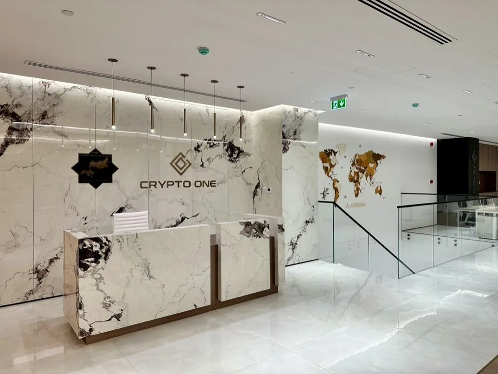 Reception at Crypto One: a book-matched marble wall with the Crypto One sign and a white stone desk