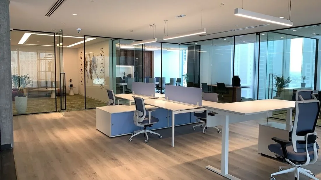 Work floor at International Materials, Opus by Omniyat: desks under linear lights, glass offices behind