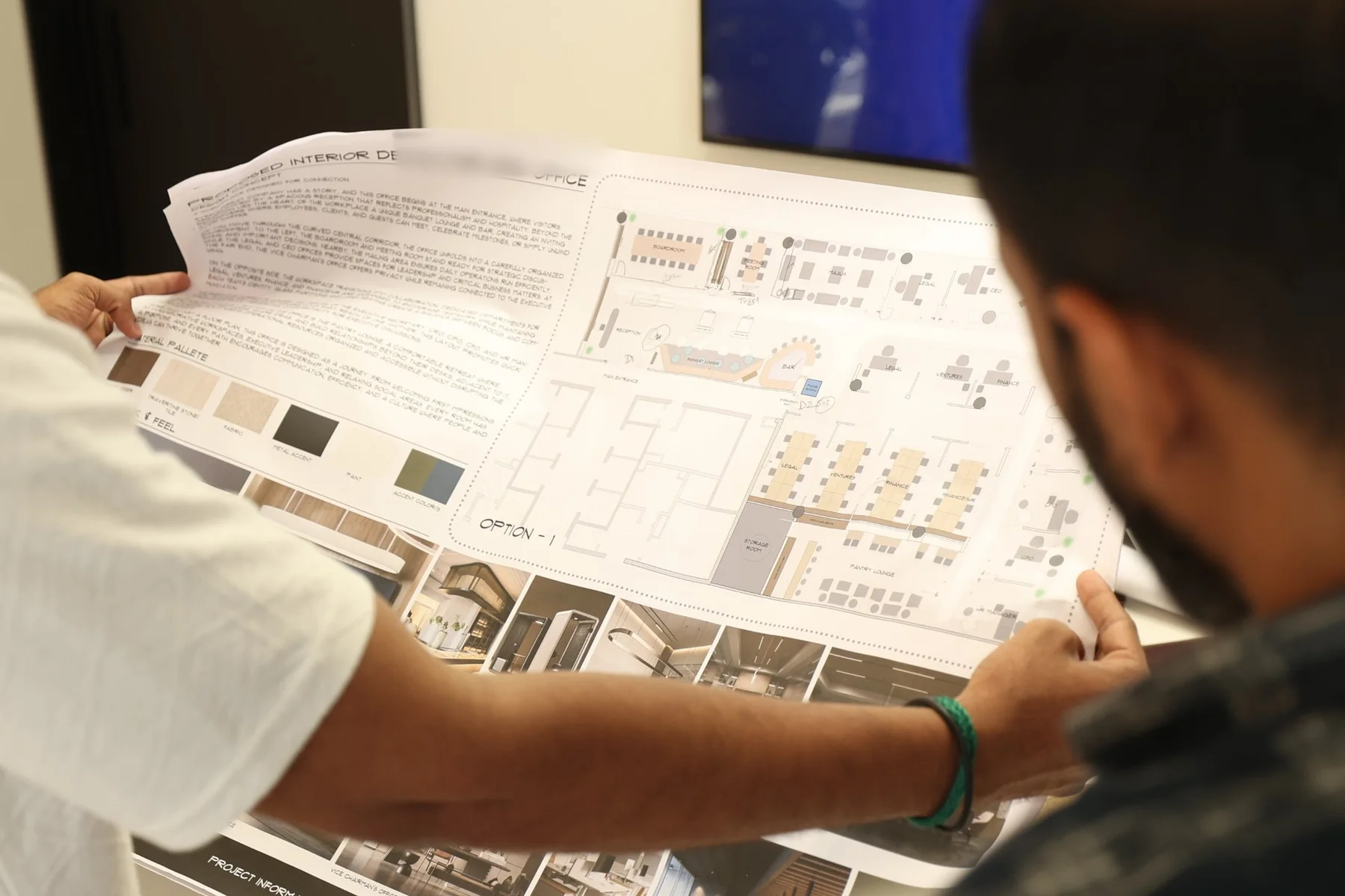 Two Fajr designers reading a printed office test fit, Option 1, with its material palette and concept notes, at the studio