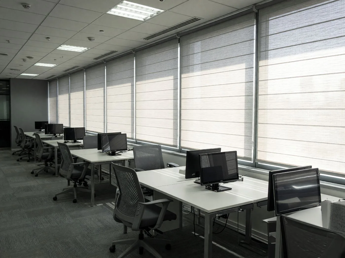 Concept visualisation: desks facing a window wall with every blind pulled down at midday and glare on the screens