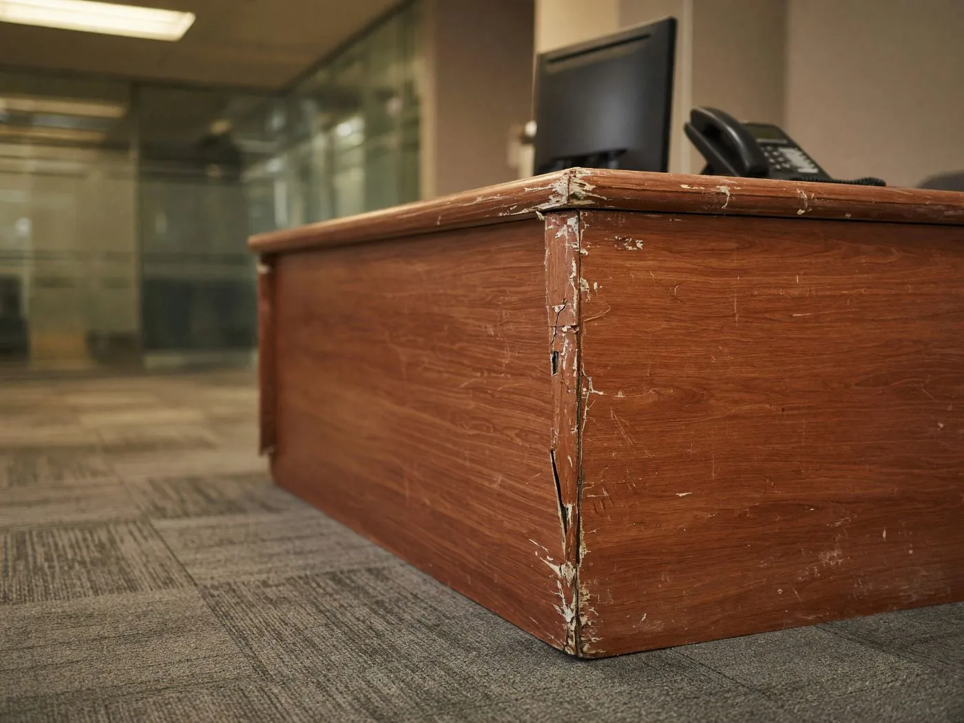 Concept visualisation: a reception counter with chipped laminate edges and carpet tiles worn flat along the walking line