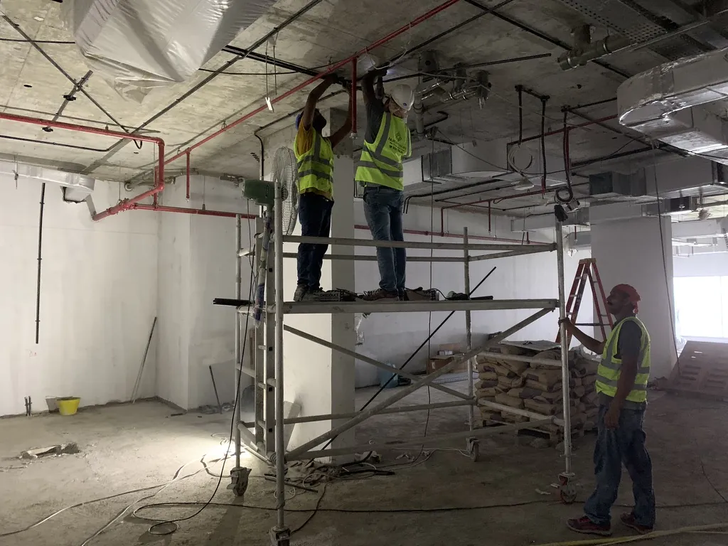 Photograph: Fajr site team fixing services overhead from a mobile scaffold on an open office floor