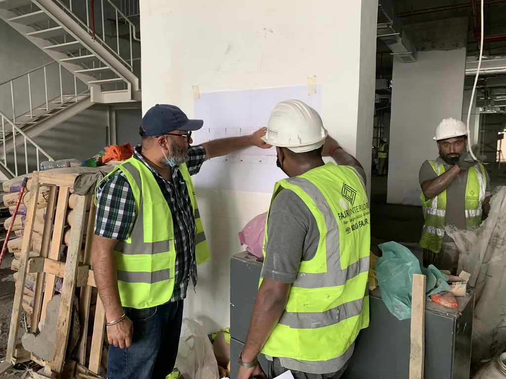 Photograph: Fajr site engineer and team reading a layout drawing taped to a column on an office floor under construction