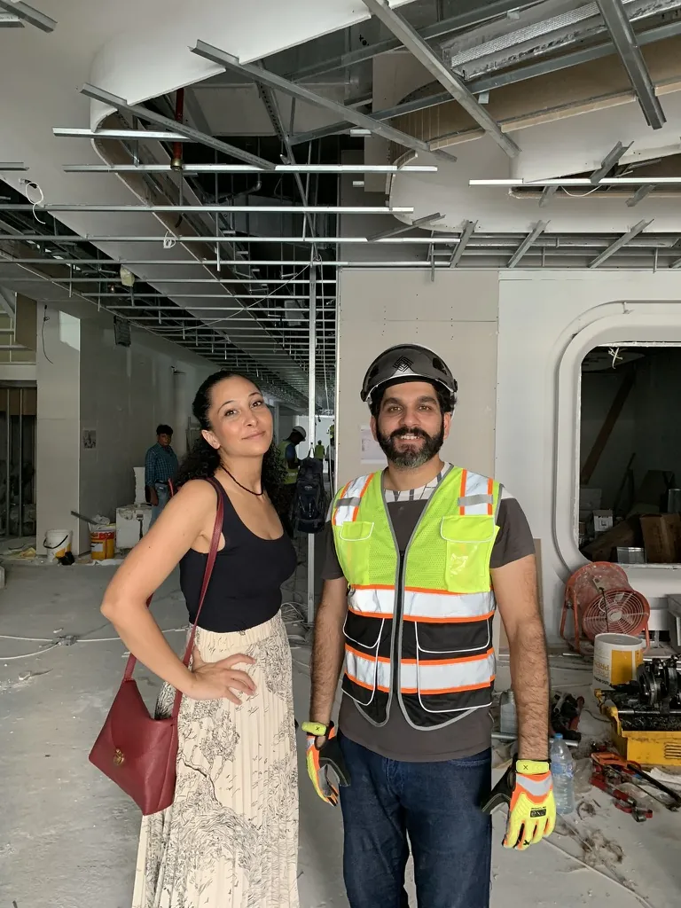 Photograph: Zeeshan Patel in Fajr hi-vis under exposed ceiling framing on an office floor under construction, a visitor beside him