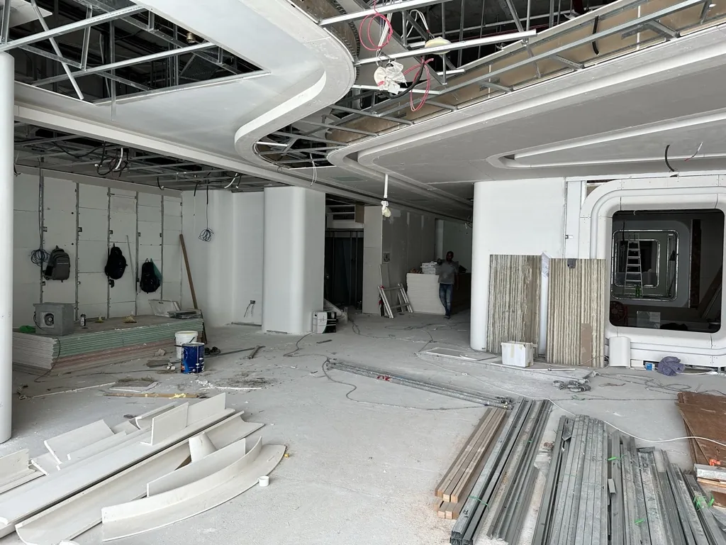 Photograph: Curved plasterboard ceiling bulkheads and boarded columns on an office floor under construction, materials stacked on the floor