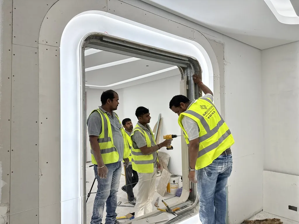 Photograph: Fajr team fixing the frame of a curved, lit portal opening in a plasterboard wall